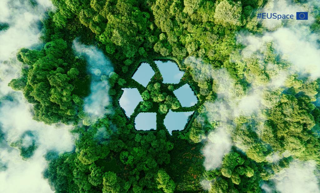 Aerial view of a dense green forest with light fog, featuring a large, stylized recycling symbol made of reflective water surfaces integrated into the landscape. In the top right corner, there is the hashtag #EUSpace alongside the European Union flag.